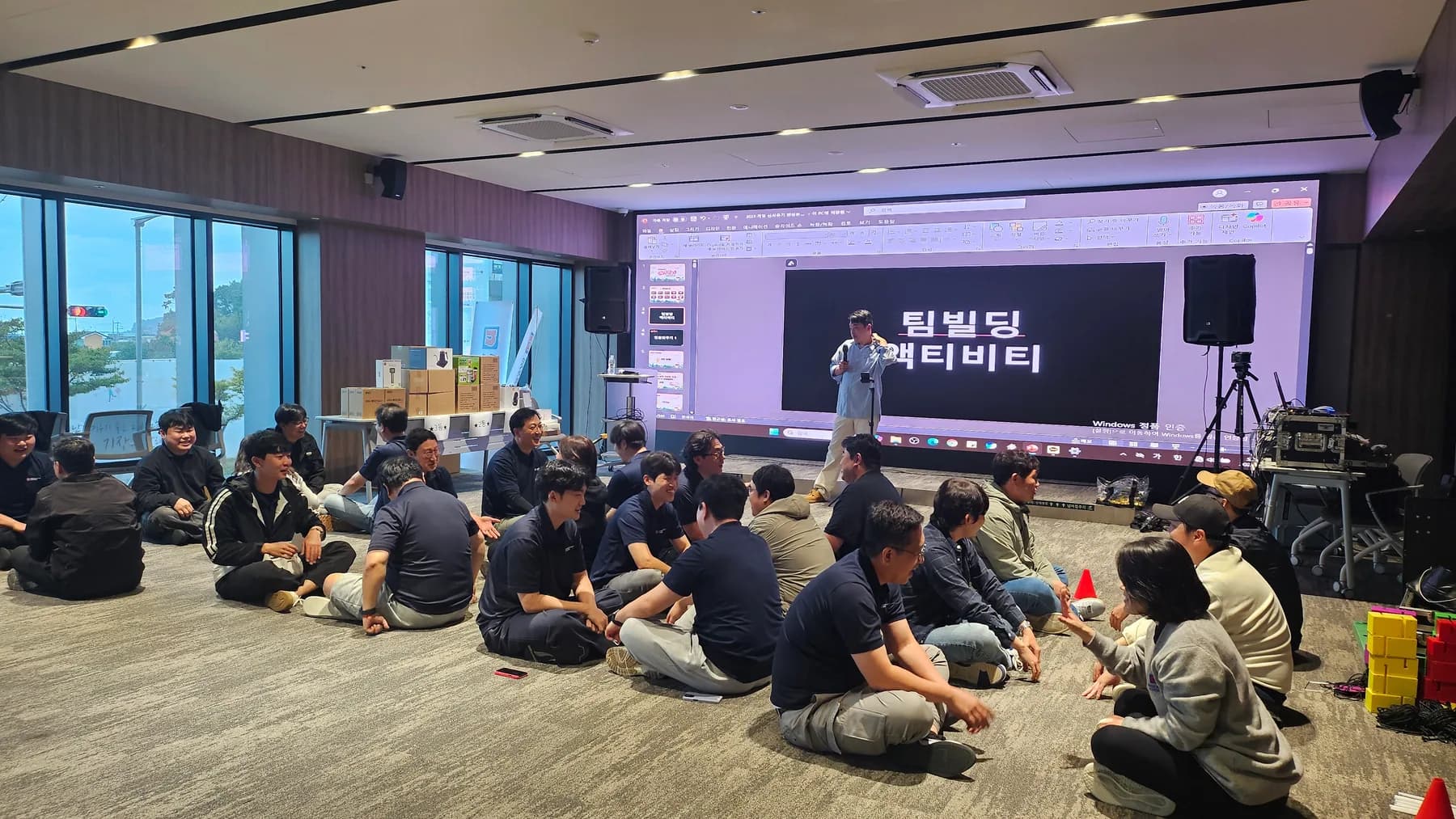 기업 참가자들이 소그룹으로 둘러앉아 전문 MC의 안내에 따라 팀빌딩 프로그램에 참여하는 실제 현장