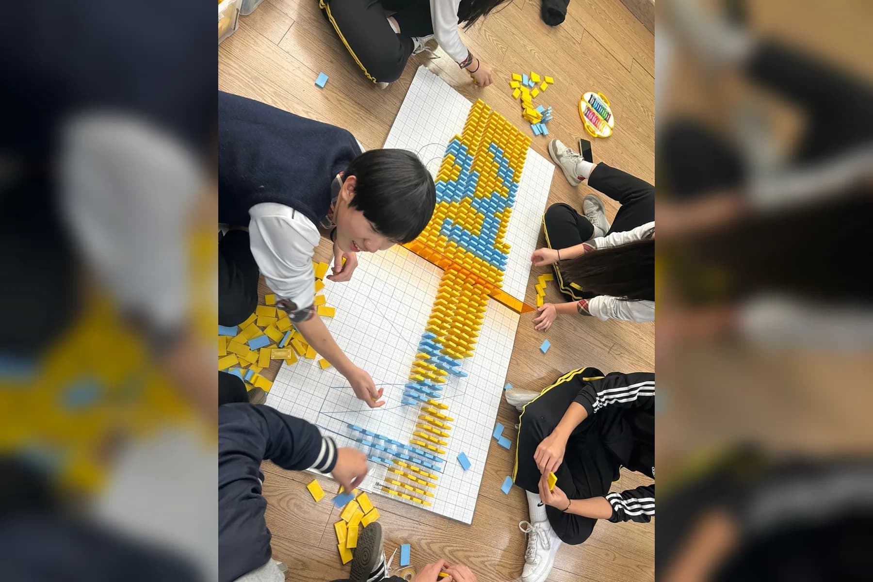 학생들이 설계 도면 위에 노란색과 파란색 도미노를 함께 세우는 실제 팀빌딩 현장