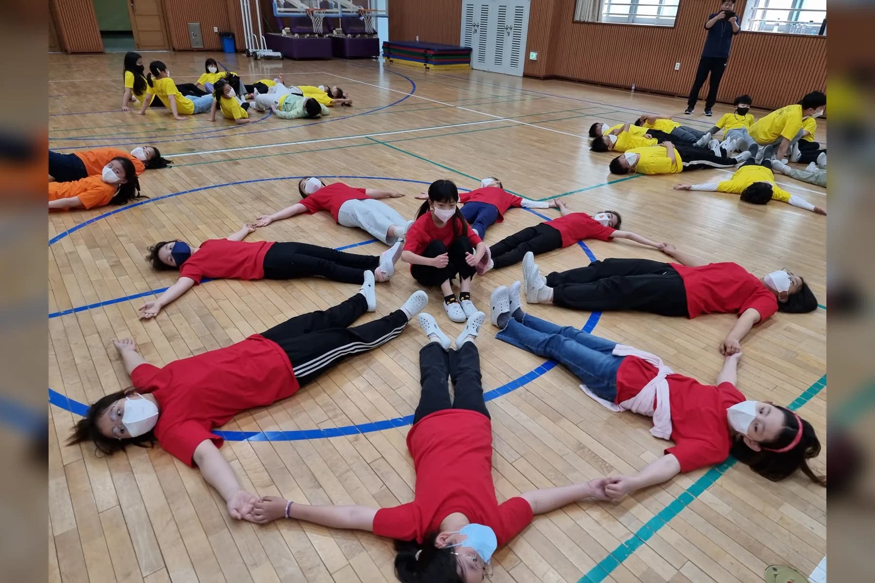 빨간색 단체복을 입은 학생들이 체육관 바닥에서 몸으로 모양을 만드는 실제 팀 미션