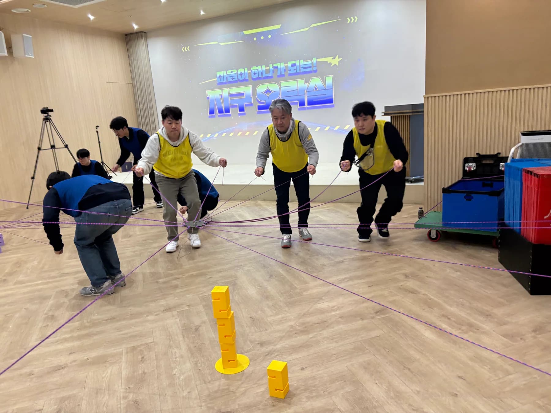 노란 팀 참가자들이 여러 줄을 함께 조작해 블록 탑을 쌓는 실제 팀빌딩 현장